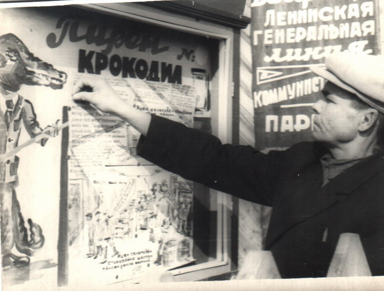 На переднем плане изображения мужчина указывает на плакат, висящий на стене. Плакат имеет...